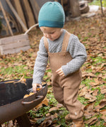 Disana organic merino wool dungarees worn by a toddler playing with leaves 