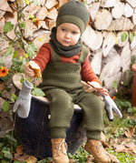 Disana organic merino wool dungarees worn by a toddler sitting on a plant pot