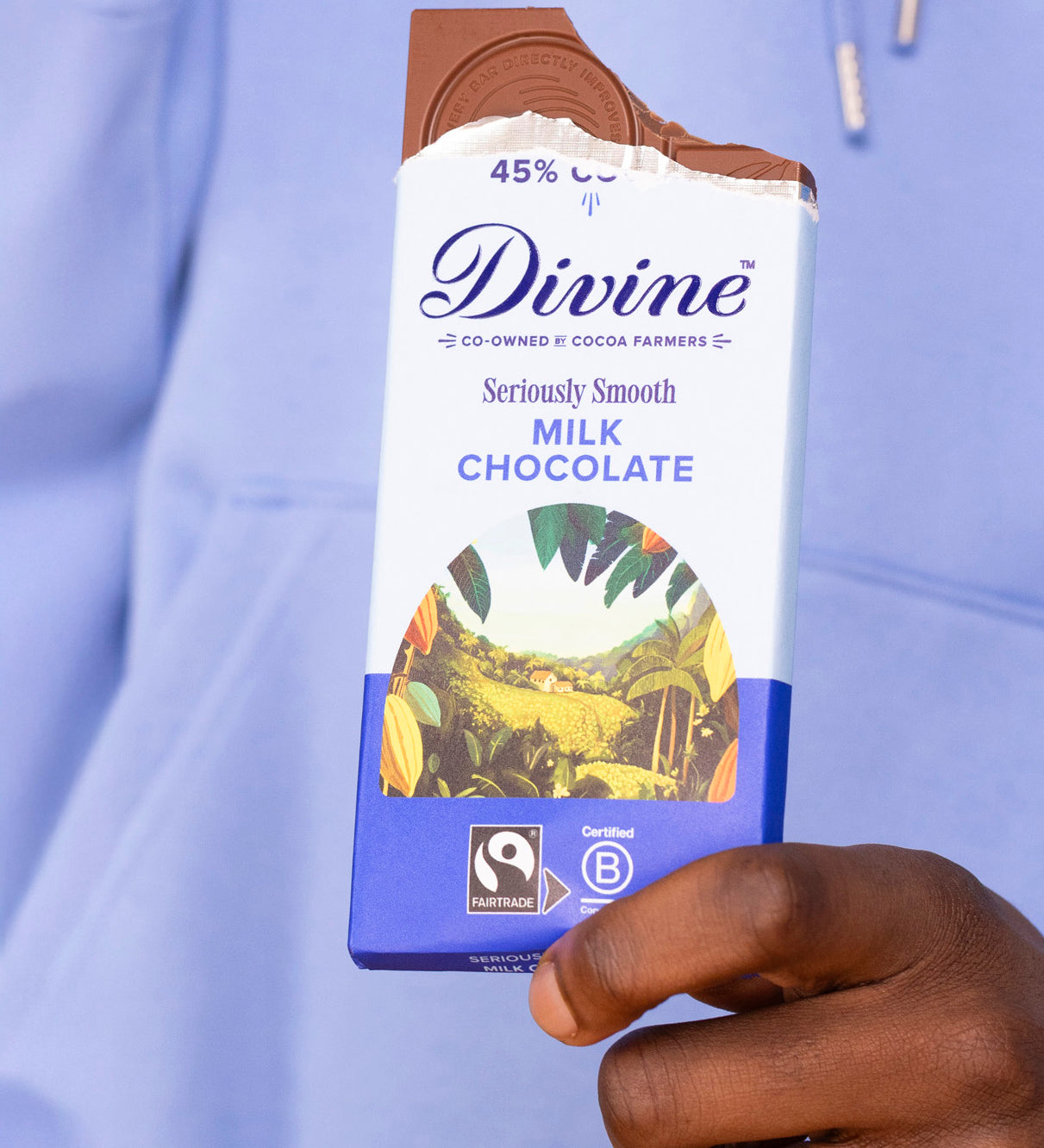 Adult hand holding the Divine fairtrade smooth milk chocolate bar with the top bitten off