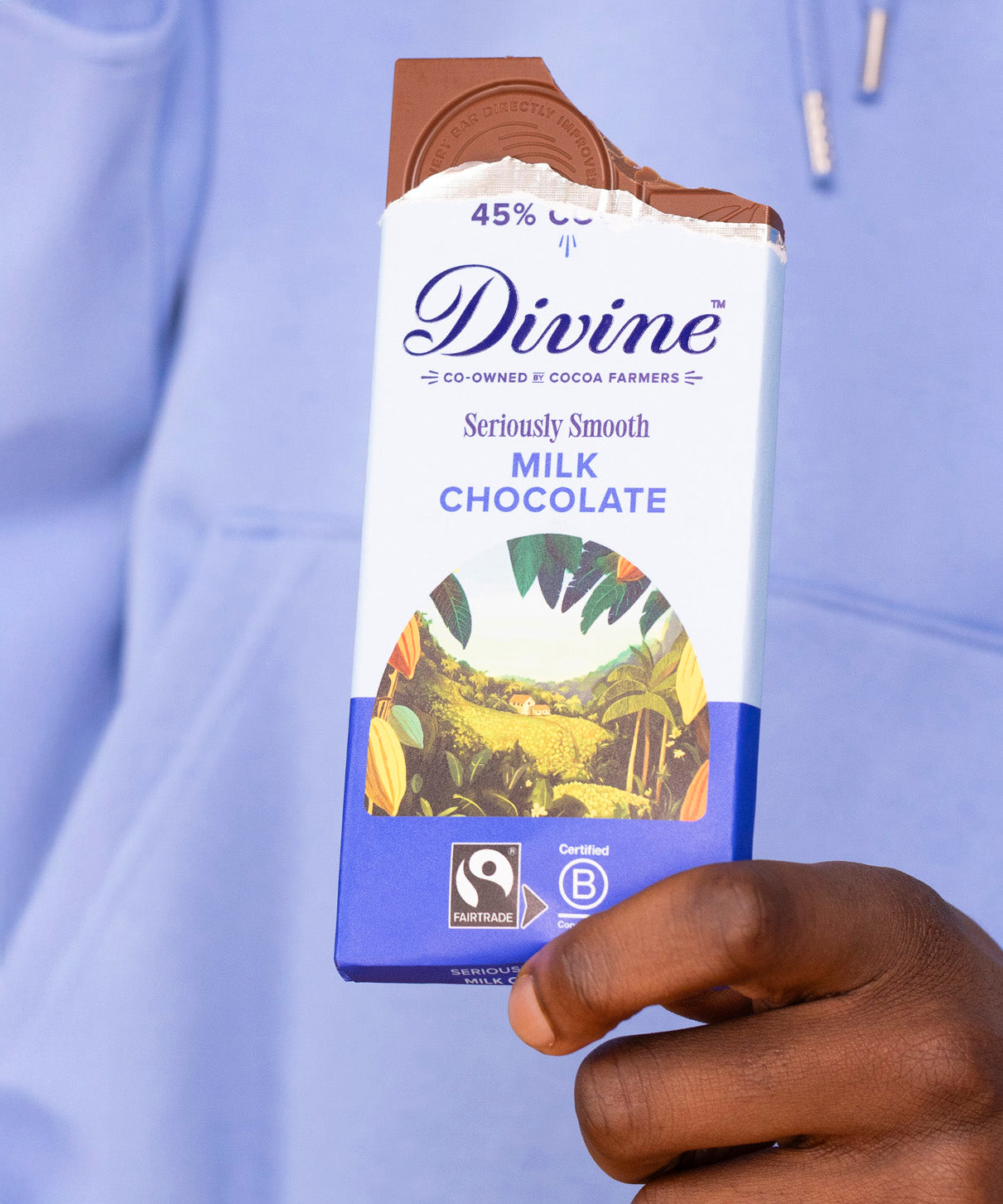 Adult hand holding the Divine fairtrade smooth milk chocolate bar with the top bitten off
