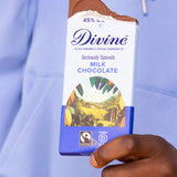 Adult hand holding the Divine fairtrade smooth milk chocolate bar with the top bitten off