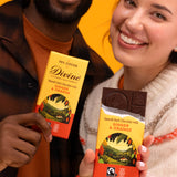 2 adults holding Divine fairtrade smooth dark chocolate with ginger and orange bars with one opened