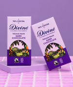 2 bars of Divine fairtrade smooth 70% dark chocolate standing on a purple platform