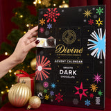Divine fairtrade dark chocolate advent calendar available at Babipur. Showing the front with an adult hand opening one of the windows. Calendar is standing in a festive inspired display.