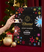 Divine fairtrade dark chocolate advent calendar available at Babipur. Showing the front with an adult hand opening one of the windows. Calendar is standing in a festive inspired display.