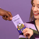 2 adults holding a Divine fairtrade smooth dark chocolate bar showing the purple wrapping with a cocoa farm illustration 