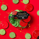 A flatlay with the Divine fairtrade dark chocolate coins inside the green netted bag and other coins scattered with a red festive inspired background. Chocolate coins available at Babipur.