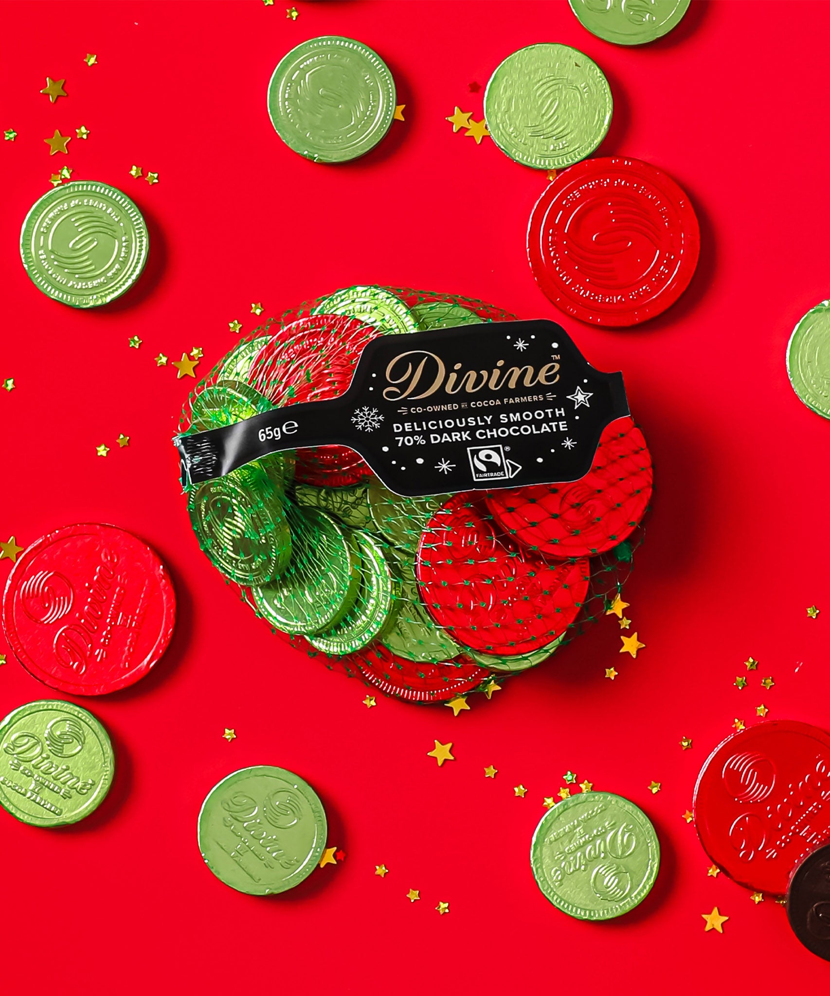 A flatlay with the Divine fairtrade dark chocolate coins inside the green netted bag and other coins scattered with a red festive inspired background. Chocolate coins available at Babipur.