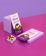 2 bard of Divine fairtrade smooth dark chocolate bar with fruit and nut resting on purple blocks with loose nuts and raisins