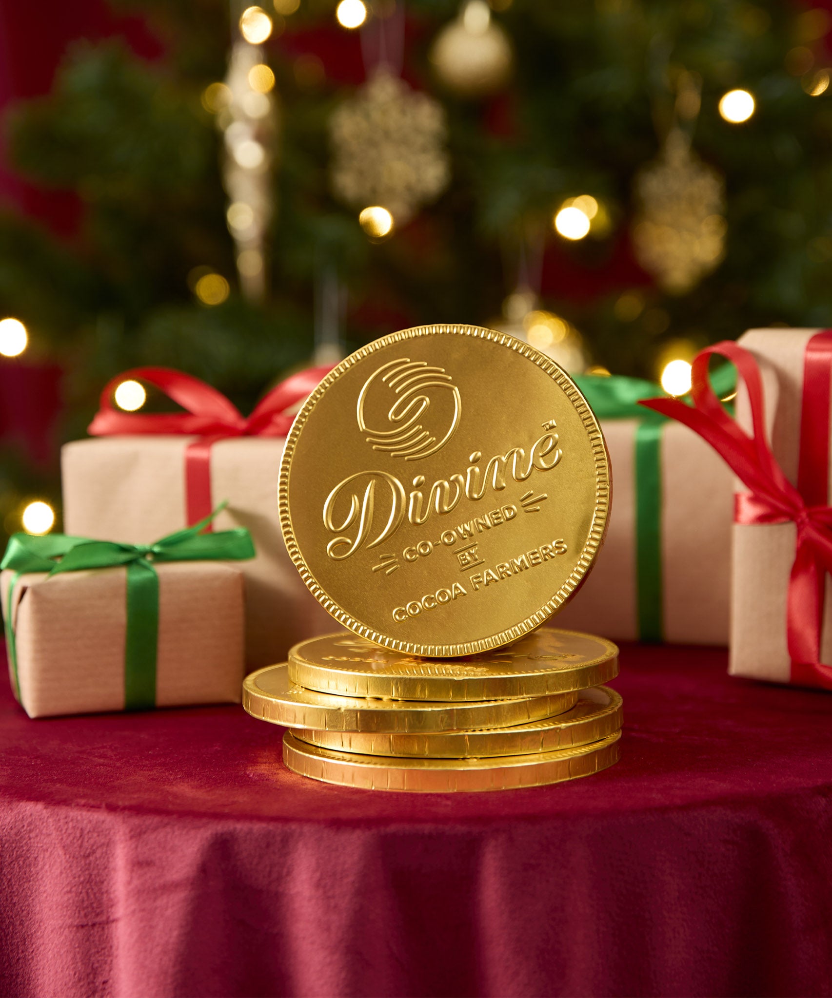 A stack of Divine fairtrade giant milk chocolate coins available at Babipur displayed with festive decorations on a red velvet table cloth