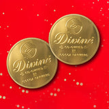 A pair of Divine fairtrade giant milk chocolate coins available at Babipur laid flat with a red festive inspired background.