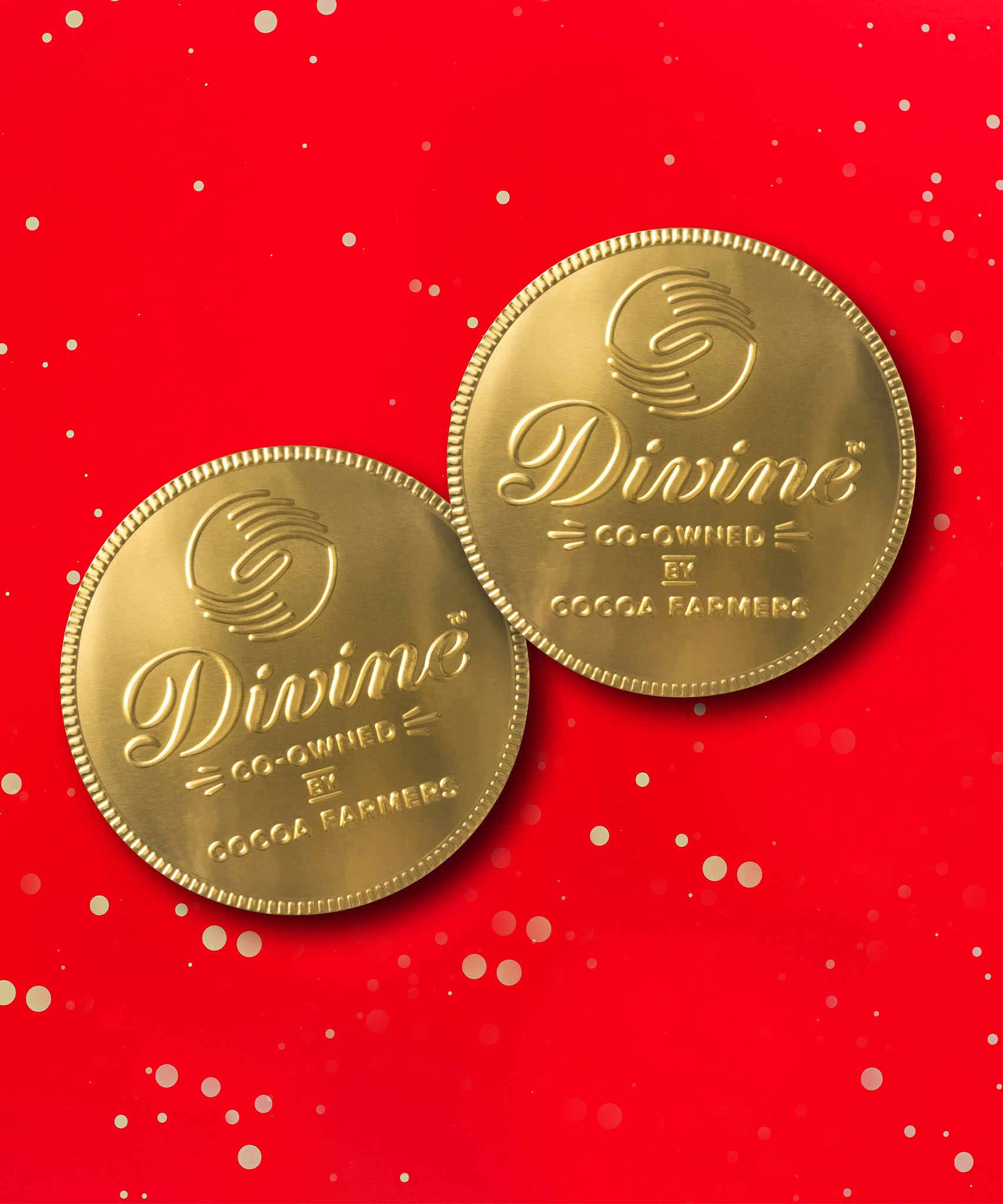 A pair of Divine fairtrade giant milk chocolate coins available at Babipur laid flat with a red festive inspired background.