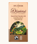 Front of Divine fairtrade smooth dark chocolate bar with hazelnut truffle in brown wrapping with a cocoa farm illustration 