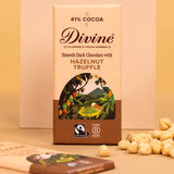 Divine fairtrade smooth dark chocolate with hazelnut truffle bar standing against platform next to loose hazelnut pieces