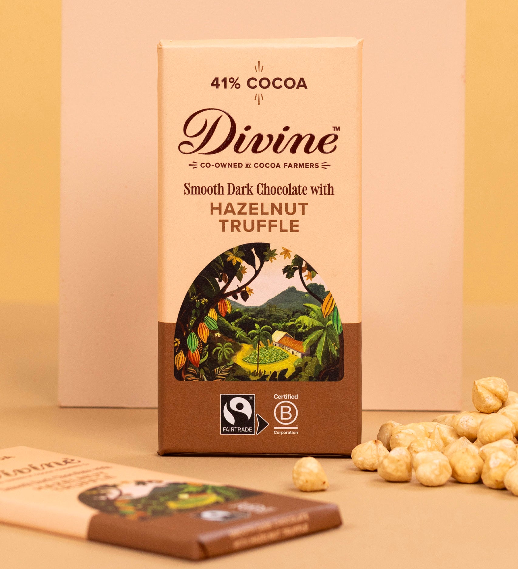 Divine fairtrade smooth dark chocolate with hazelnut truffle bar standing against platform next to loose hazelnut pieces