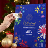 Divine fairtrade milk chocolate advent calendar available at Babipur. Showing the front with an adult hand opening one of the windows. Calendar is standing in a festive display.