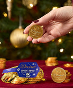 A adult hand holding one coin from the Divine fairtrade milk chocolate bag available at Babipur showing the scale of one coin.