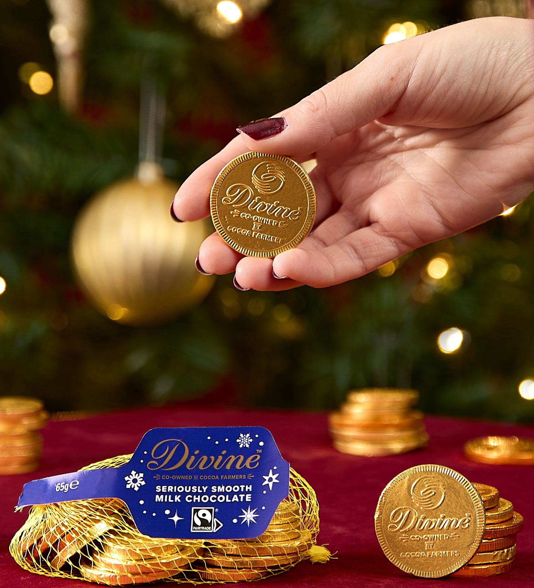 A adult hand holding one coin from the Divine fairtrade milk chocolate bag available at Babipur showing the scale of one coin.