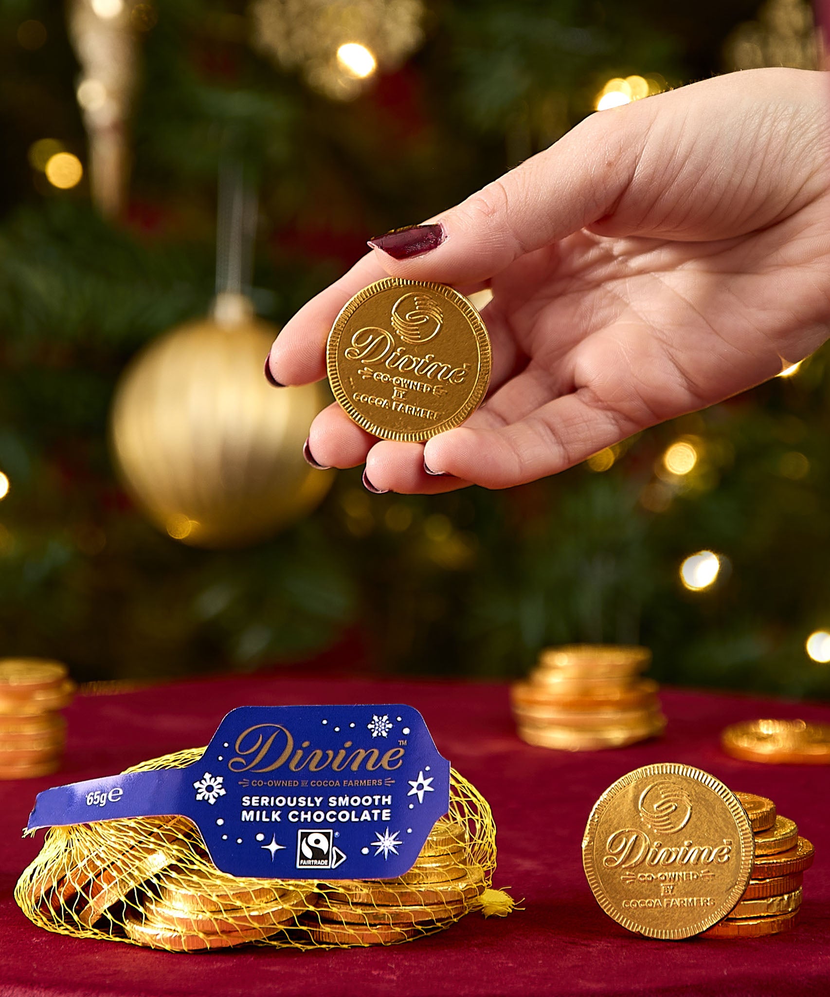 A adult hand holding one coin from the Divine fairtrade milk chocolate bag available at Babipur showing the scale of one coin.