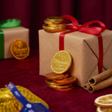 A stack of Divine fairtrade milk chocolate coins against a Christmas present. Coins available at Babipur.