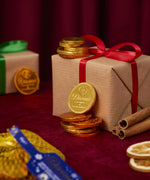 A stack of Divine fairtrade milk chocolate coins against a Christmas present. Coins available at Babipur.