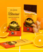 2 bars of Divine fairtrade smooth dark chocolate with ginger and orange standing upright next to loose oranges 