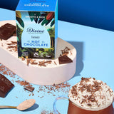 Divine fairtrade luxury hot chocolate box standing on a white platform next to a mug and shredded chocolate