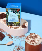 Divine fairtrade luxury hot chocolate box standing on a white platform next to a mug and shredded chocolate