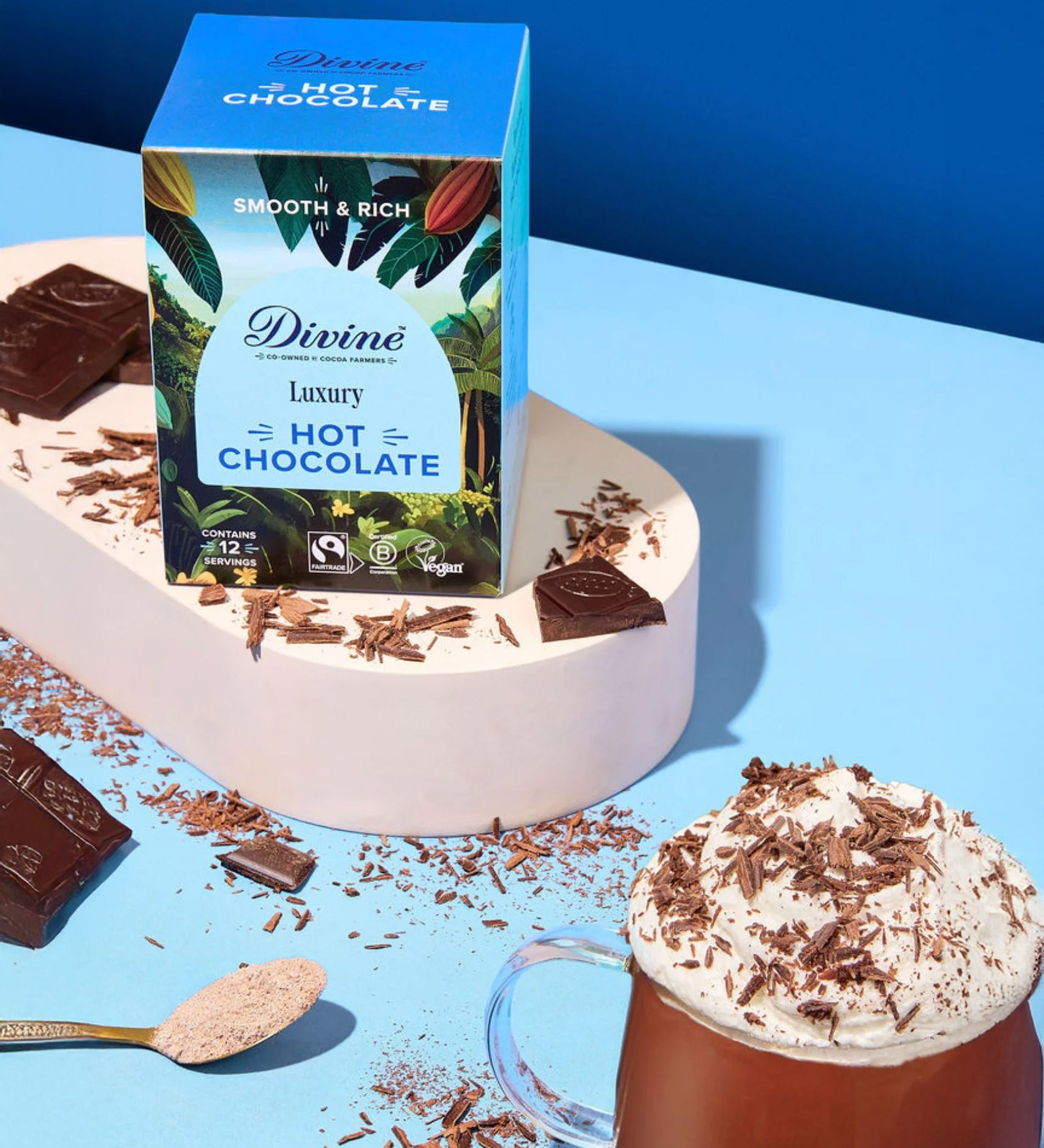 Divine fairtrade luxury hot chocolate box standing on a white platform next to a mug and shredded chocolate