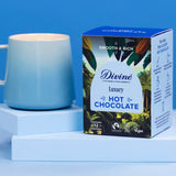 Divine fairtrade luxury hot chocolate box standing on a light blue platform next to a mug.