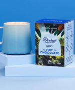 Divine fairtrade luxury hot chocolate box standing on a light blue platform next to a mug.