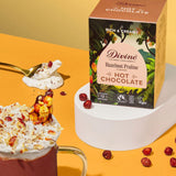 Divine fairtrade luxury hot chocolate with Hazelnut box standing on a white platform next to a mug loose hazelnut pieces