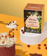 Divine fairtrade luxury hot chocolate with Hazelnut box standing on a white platform next to a mug loose hazelnut pieces