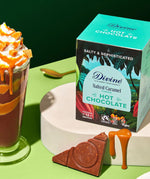 Divine fairtrade salted caramel flavour hot chocolate box standing on a white platform next to a tall glass