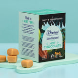 Divine fairtrade salted caramel flavour hot chocolate box standing on a mint green platform next to pieces of caramel