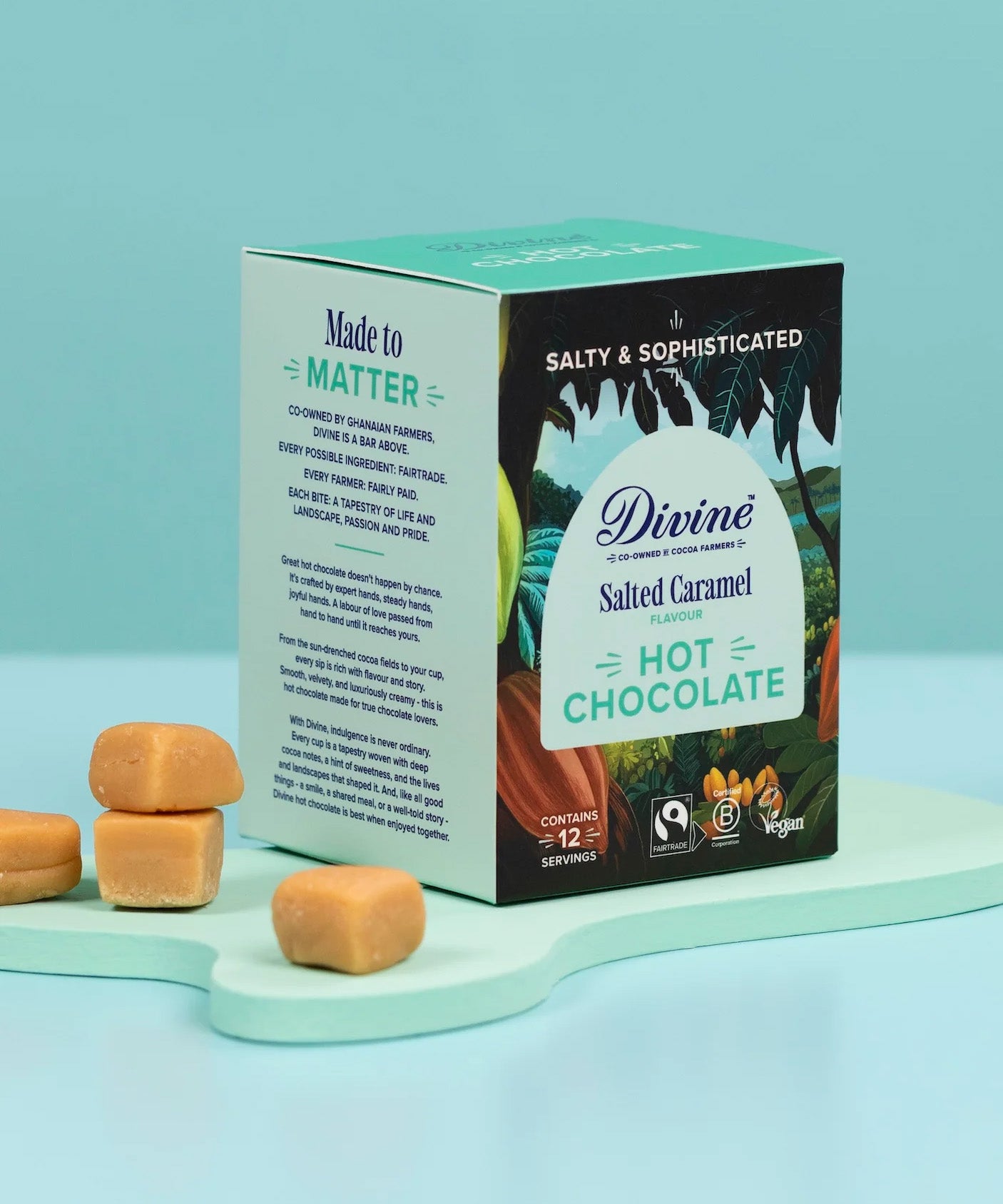 Divine fairtrade salted caramel flavour hot chocolate box standing on a mint green platform next to pieces of caramel