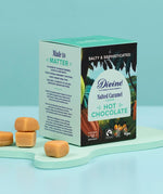 Divine fairtrade salted caramel flavour hot chocolate box standing on a mint green platform next to pieces of caramel