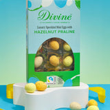 Divine Fairtrade milk chocolate mini eggs with hazelnut praline displayed in a decorated blue and green box standing on a white platform