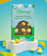Divine Fairtrade milk chocolate mini eggs with hazelnut praline displayed in a decorated blue and green box standing on a white platform
