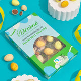 Divine Fairtrade milk chocolate mini eggs with hazelnut praline displayed in a decorated blue and green box lying flat on a blue surface