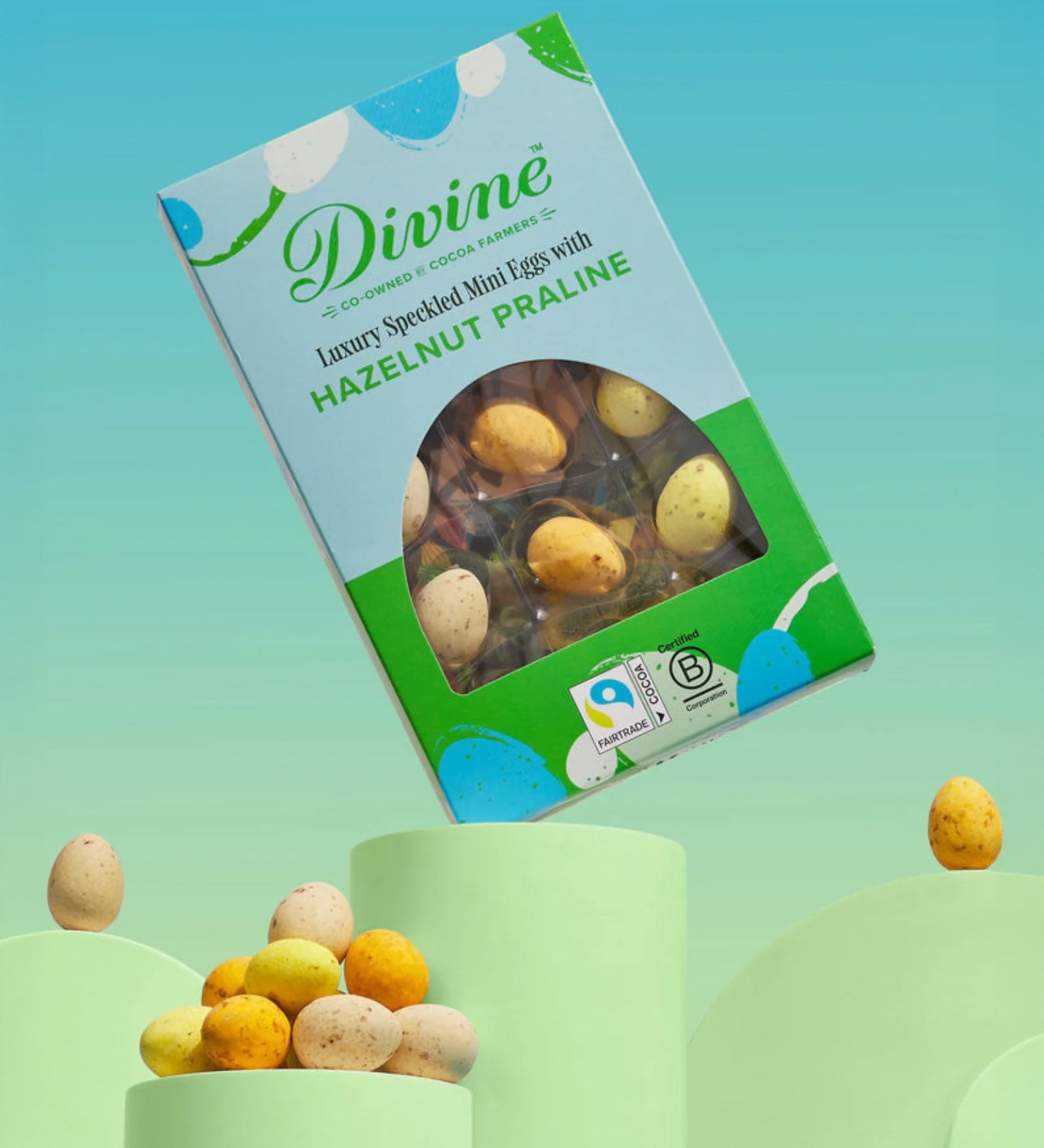 Divine Fairtrade milk chocolate mini eggs with hazelnut praline displayed in a decorated blue and green box balancing on a green platform 