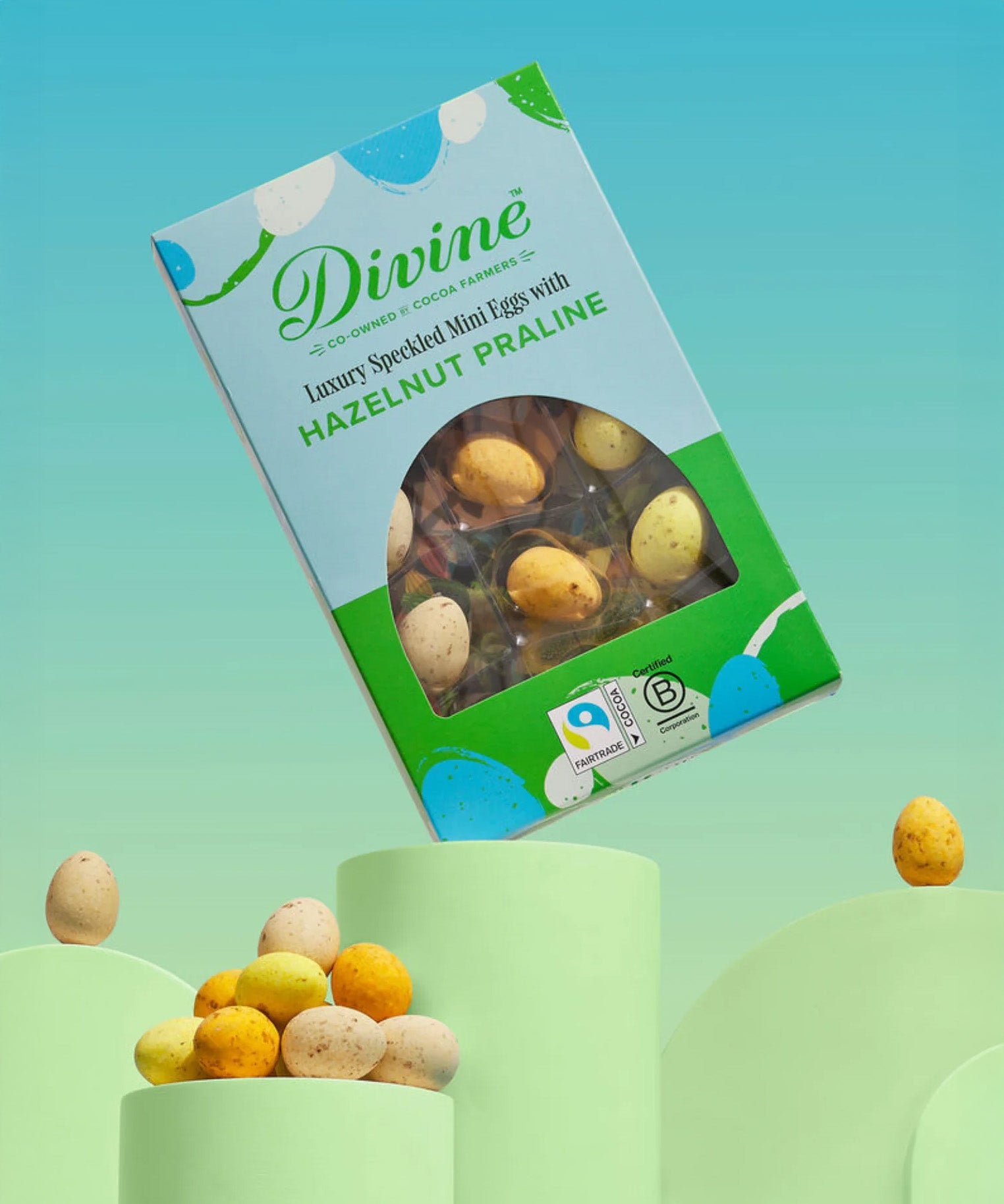 Divine Fairtrade milk chocolate mini eggs with hazelnut praline displayed in a decorated blue and green box balancing on a green platform 