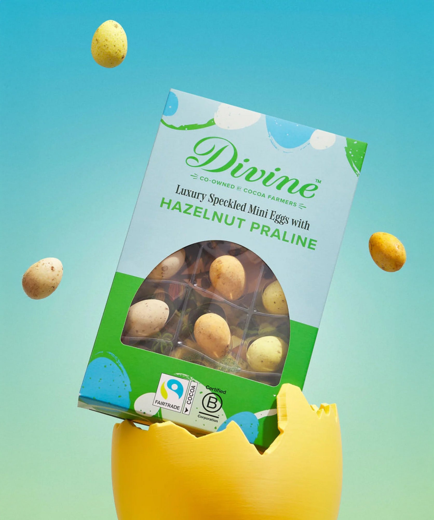Divine Fairtrade milk chocolate mini eggs with hazelnut praline displayed in a decorated blue and green box standing in a broken yellow egg