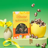 Divine Fairtrade milk chocolate mini eggs with smooth caramel displayed in a decorated yellow and orange box standing next to a broken egg filled with mini eggs