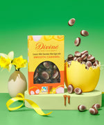 Divine Fairtrade milk chocolate mini eggs with smooth caramel displayed in a decorated yellow and orange box standing next to a broken egg filled with mini eggs
