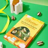 Divine Fairtrade milk chocolate mini eggs with smooth caramel displayed in a decorated yellow and orange box lying flat on a green surface 