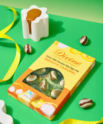 Divine Fairtrade milk chocolate mini eggs with smooth caramel displayed in a decorated yellow and orange box lying flat on a green surface 