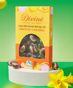Divine Fairtrade milk chocolate mini eggs with smooth caramel displayed in a decorated yellow and orange box standing on a white block next to daffodils