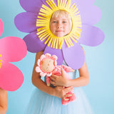 Child holding Olli Ella Dozy Dinkum Doll in Fuchsia Twinkle, wearing a soft pink velour onesie with a flower-shaped hood, available at Babipur.