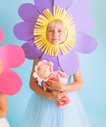 Child holding Olli Ella Dozy Dinkum Doll in Fuchsia Twinkle, wearing a soft pink velour onesie with a flower-shaped hood, available at Babipur.
